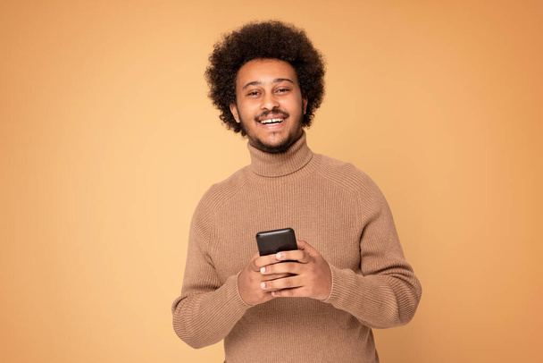 Smiling african american man using mobile phone in studio. People lifestyle concept.  - 写真・画像