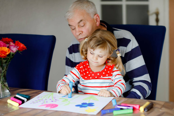 Menina bebê pequeno bonito e bonito avô sênior pintura com canetas de feltro coloridas e lápis em casa. Neto e homem se divertindo juntos, família criativa. - Foto, Imagem