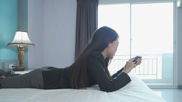 Smiling Asian Thai business woman using a smartphone or mobile phone in bedroom at hotel in technology device concept. Lifestyle people. - Fotografie, Obrázek