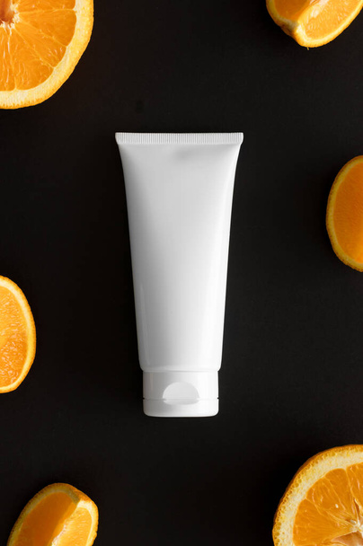 Top view of a tube of cream surrounded by oranges on a black background. - Фото, зображення