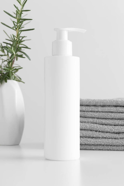 White cosmetic shampoo dispenser bottle mockup with towels and a rosemary  on a white table. - Foto, afbeelding