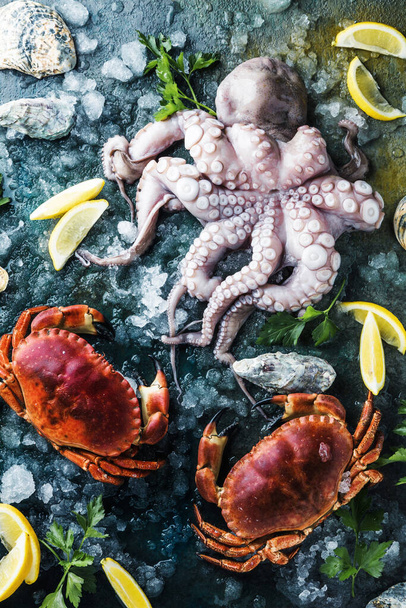 top view of delicious seafood with crabs, oysters, octopus, lemon slices, herbs and ice on dark surface - Foto, Bild