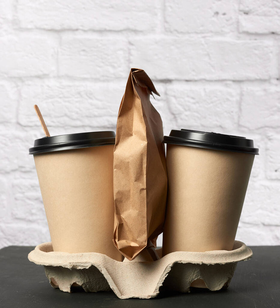 dos vasos desechables de papel marrón con un soporte de tapa de plástico en la bandeja, fondo blanco, recipientes para llevar - Foto, imagen