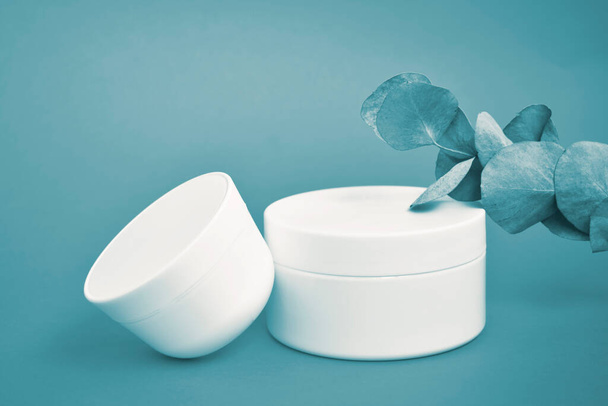 Pot cosmétique rond, blanc, en plastique, disposition isolée sur fond bleu. - Photo, image