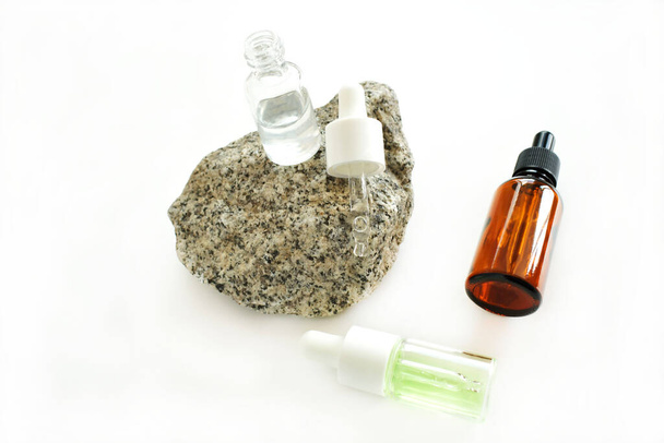 Butelki kosmetyczne z pipetą z olejkiem eterycznym w różnych słoikach, naturalnym kamieniem i kwiatami na białym tle. Medycyna alternatywna i kosmetyki. - Zdjęcie, obraz