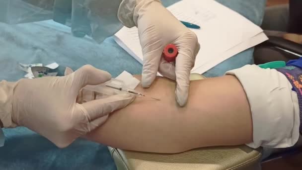 Egy nővér a kórházban vért vesz egy beteg vénájából, hogy ellenőrizze a koronavírus közelről. Tudományos mikrobiológiai vizsgálat. Tű a vénában. Vérvételi pumpa. COVID-19 szám - Felvétel, videó