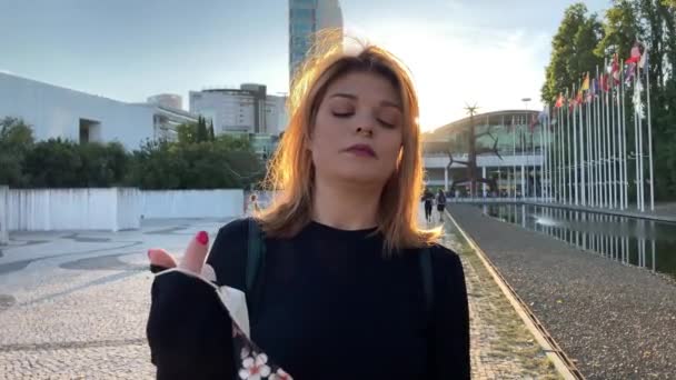 4k zpomalené záběry mladé krásné ženy s obličejovou maskou proti propuknutí Covid-19 v Lisabonu (Portugalsko). Pohled na hravou dívku kráčející venku s vlajkovými stožáry vzadu - Záběry, video