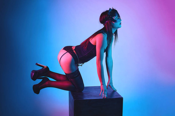 attractive girl in a cat mask on a black cube. - Foto, afbeelding
