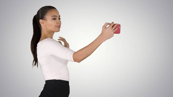 Pretty girl taking a selfie and walking on gradient background. - Foto, Imagem
