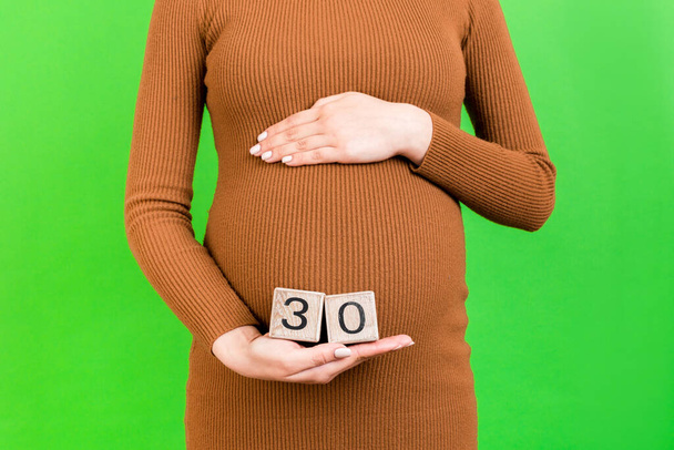 Zbliżenie obraz trzydziestu tygodni ciąży kostki w rękach kobiety w ciąży na zielonym tle. Szczęśliwej ciąży. Przestrzeń kopiowania. - Zdjęcie, obraz