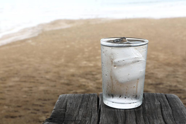 Пейте воду с холодным льдом в стакане воды на старой деревянной доске на пляже. - Фото, изображение