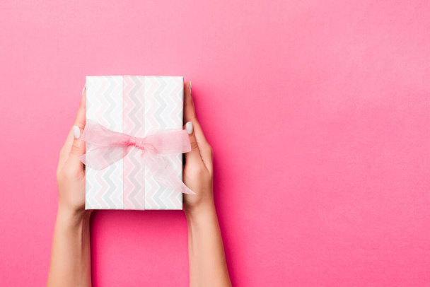 Girl Hands holding craft paper gift box with as a present for Christmas or other holiday on pink background, top view with copy sppace. - 写真・画像