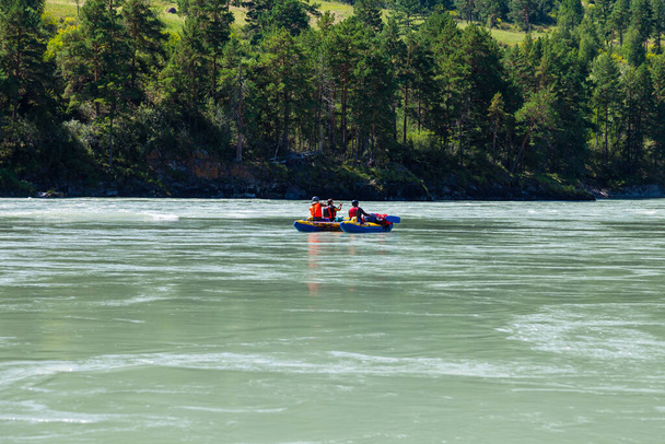 Grupo de turistas que descansan en Altai y rafting río abajo de la montaña - Katuni turquesa en azul bote de goma inflable en chalecos amarillos protectores especiales contra el fondo de la orilla verde con árboles - Foto, Imagen