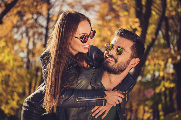 Photo of positive couple guy hug piggyback his girlfriend in september city town sunshine forest wear casual jackets - Фото, изображение