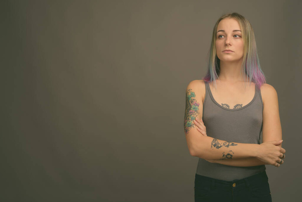 Studio shot of young beautiful rebellious woman with multicolored hair against gray background - Photo, image