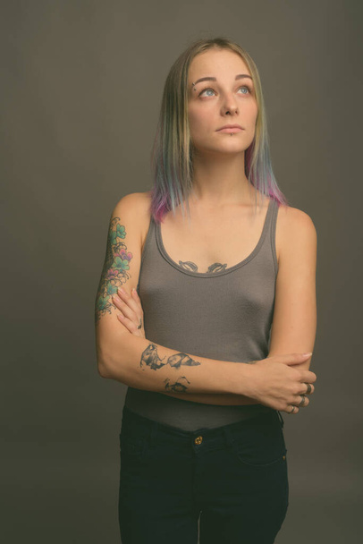 Studio shot of young beautiful rebellious woman with multicolored hair against gray background - Photo, Image