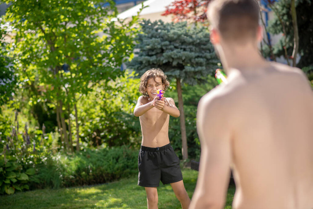 Boy with water pistol aiming at man - 写真・画像
