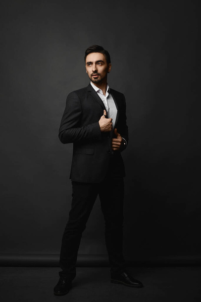 Full-length portrait of a handsome bearded gentleman in a black suit on the dark background. - Zdjęcie, obraz