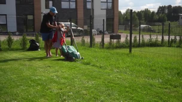 Poco ayudante niña hija cortar césped con su papá hombre en el patio de la casa - Imágenes, Vídeo