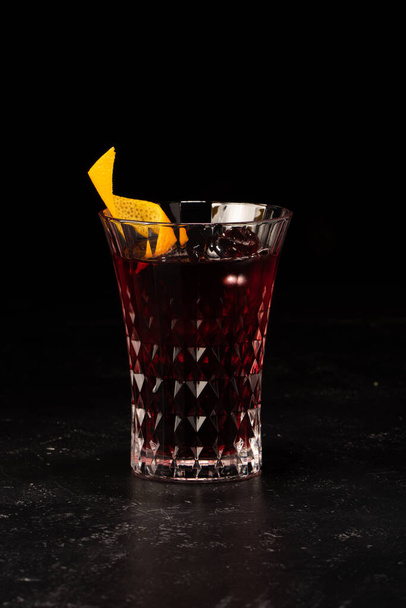 Cóctel alcohólico con jarabe de bayas y decoración de cáscara de naranja en un pequeño vaso facetado - Foto, Imagen