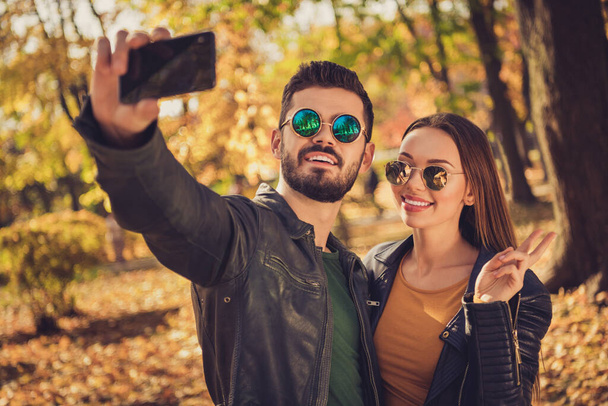 Photo of two people students girl guy take selfie on cellphone make v-sign in fall september season park wear glasses jacket - Zdjęcie, obraz