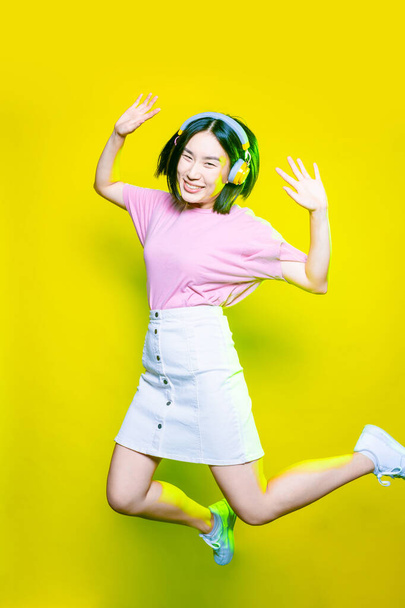 Молода азіатська жінка стрибає на жовтому фоні слухаючи музику - Захоплена молода енергійна азіатка насолоджується музикою ізольовано - захоплюється, насолоджується, розважається концепцією
 - Фото, зображення