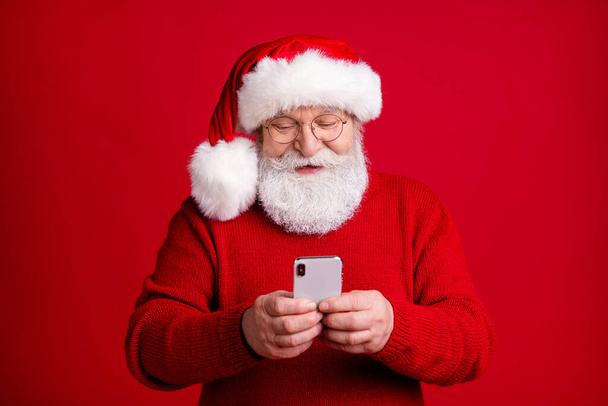 Photo old retired pensioner grey hair man in santa claus headwear use smartphone follow social media x-mas holly jolly discounts wear sweater jumper isolated bright shine color background - 写真・画像