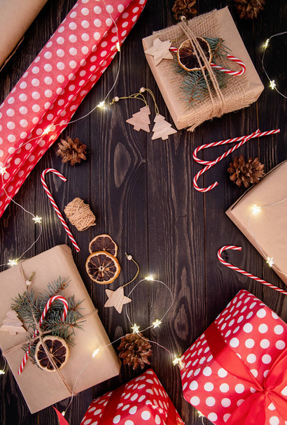 Envoltura de regalos de Navidad. Cajas de regalo envueltas en papel artesanal decorado con conos de pino, bastones de caramelo y ramas de abeto vista superior plana sobre fondo de madera oscura - Foto, Imagen