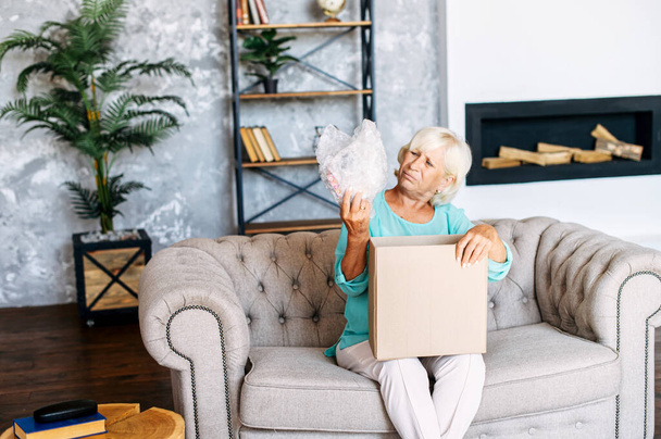 Senior woman is unpacking a cardboard box - Фото, зображення