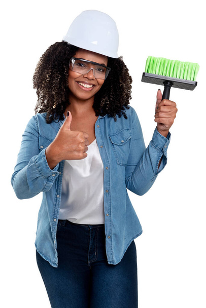 Neşeli ve gülümseyen Brezilyalı siyah kadın, beyaz arka planda izole edilmiş, kafasında gözlük ve başlık takan bir fırçayla çalışıyor.. - Fotoğraf, Görsel
