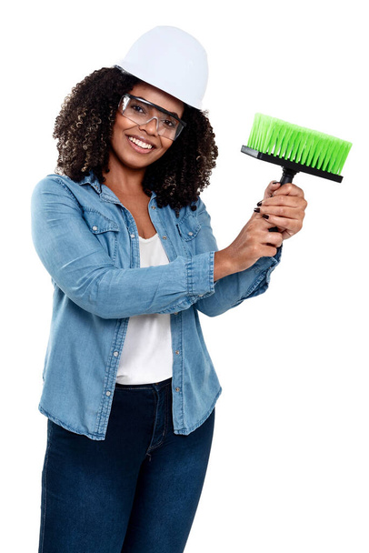 Mujer negra brasileña alegre y sonriente aislada sobre fondo blanco, trabajando con un cepillo con gafas y casco en la cabeza. - Foto, Imagen