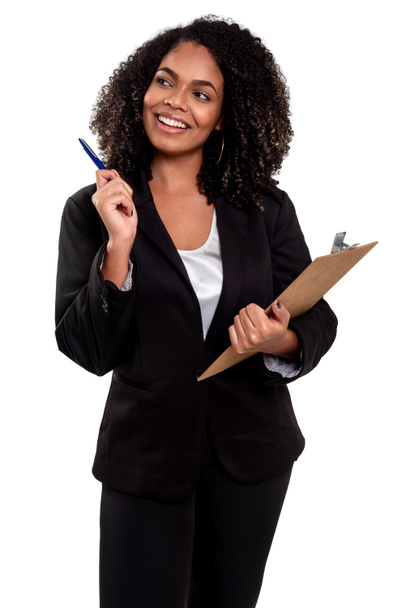 Χαρούμενη και χαμογελαστή εκτελεστική μαύρη Βραζιλιάνα γυναίκα απομονωμένη σε λευκό φόντο, δουλεύοντας με ένα πρόχειρο και κρατώντας ένα στυλό. - Φωτογραφία, εικόνα