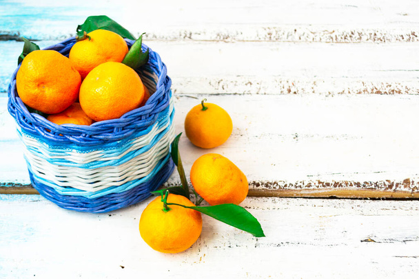 Citrus tangerines lie in a white and blue basket on a white wooden background. Christmas concept. Copy of space. - Fotó, kép