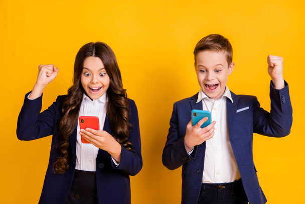 Portrait of attractive addicted glad cheerful small little schoolkids using gadget having fun playing web app game leisure free time isolated bright vivid shine vibrant yellow color background - Foto, Imagen