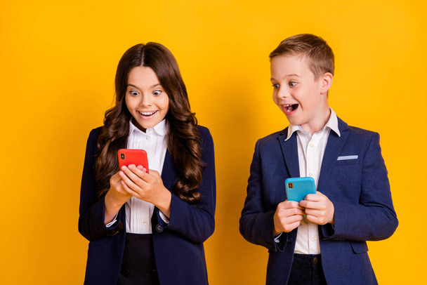 Portrait of attractive addicted glad excited cheerful small little schoolkids using gadget having fun media multimedia like repost share isolated bright vivid shine vibrant yellow color background - Foto, Imagen