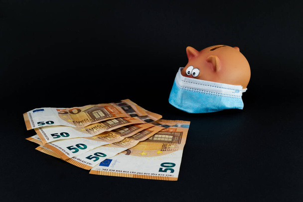 Pig piggy bank figure with sanitary mask in times of Covid in front of euro banknotes - Valokuva, kuva