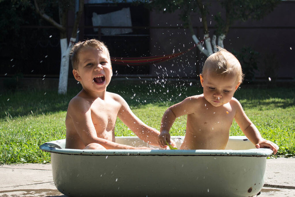 Ένας αδερφός παίζει με την μικρή αδελφή στο μπάνιο στην πίσω αυλή. - Φωτογραφία, εικόνα