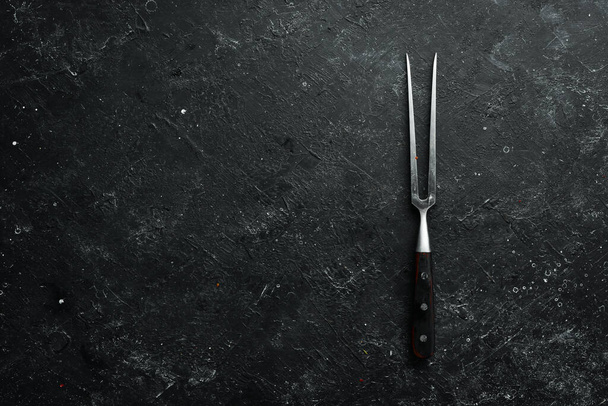 Fork for steak on a black stone background. Top view. Rustic style. - Zdjęcie, obraz