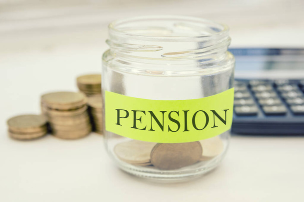 Text label "Pension" on full coins in a jar. concept of savings, donation, financial, future investment and insurance.Coins and calculator. - 写真・画像