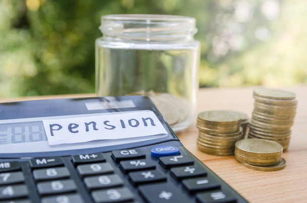 Concepto de pensiones. Monedas y calculadora sobre una mesa de madera. Pegatina con la palabra "pensión" - Foto, Imagen