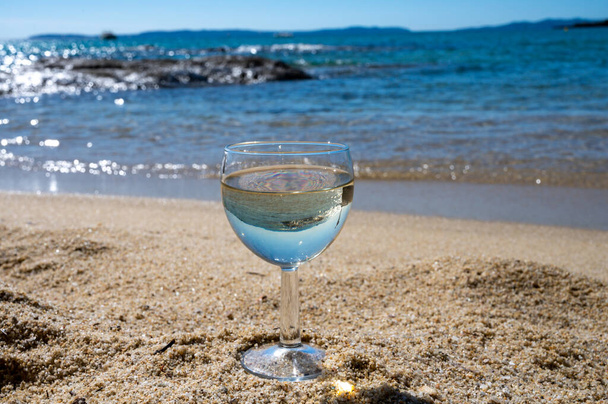 Copa de vino blanco seco local en la playa de arena blanca y el mar Mediterráneo azul en el fondo, cerca de Le Lavandou, Var, Provenza, Francia - Foto, imagen