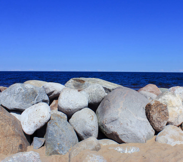 μια καθαρή ηλιόλουστη μέρα του καλοκαιριού δίπλα στη θάλασσα ή στη λίμνη. μεγάλες πέτρες στην ακτή και γαλανός καθαρός ουρανός - Φωτογραφία, εικόνα
