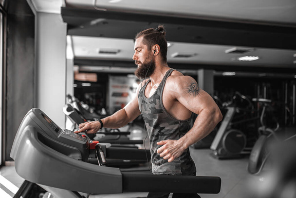 Adult strong bearded man running on treadmill in gym - Фото, зображення