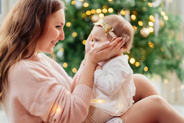 mother and daughter sitting at Christmas tree.  - Foto, afbeelding