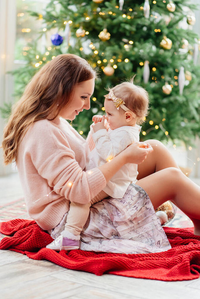 mother and daughter sitting at Christmas tree.  - Photo, image