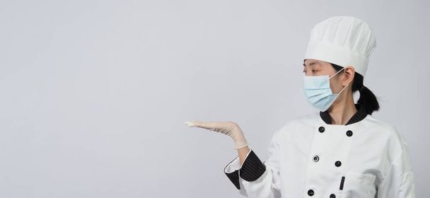 Aziatische vrouwelijke chef-kok in witte kleur uniform met hygiënische zoals medische gezichtsmasker en rubber handschoen voor het voorkomen of beschermen van covid-19 of coronavirus pandemie. Studio shot en kopieer ruimte. - Foto, afbeelding