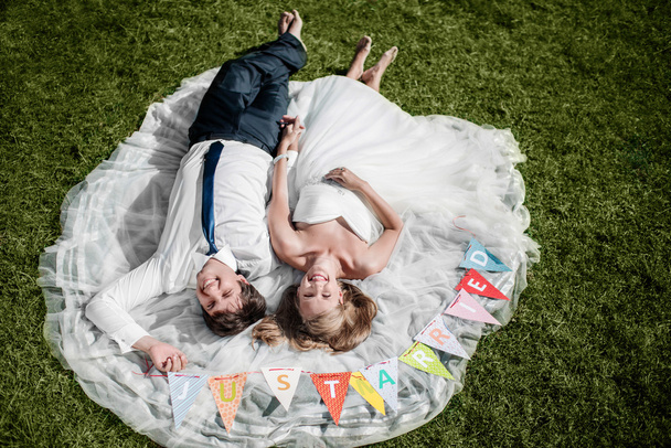 усміхнена весільна пара лежить на траві з "просто одруженим" фл
 - Фото, зображення
