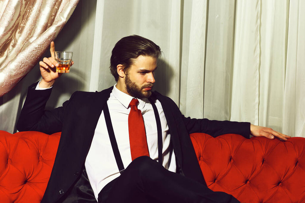 bearded man, businessman holding glass of whiskey in red tie - Fotó, kép