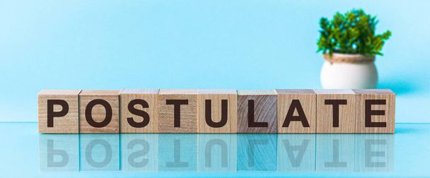 La palabra postulado hecho de letras de madera marrón se encuentra en una mesa azul - Foto, Imagen