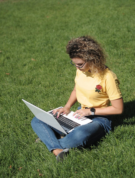 Dışarıda dizüstü bilgisayarı olan genç bir kadın. Çevrimiçi eğitim, uzaklık eğitimi öğrencisi dizüstü bilgisayarla çalışıyor. - Fotoğraf, Görsel
